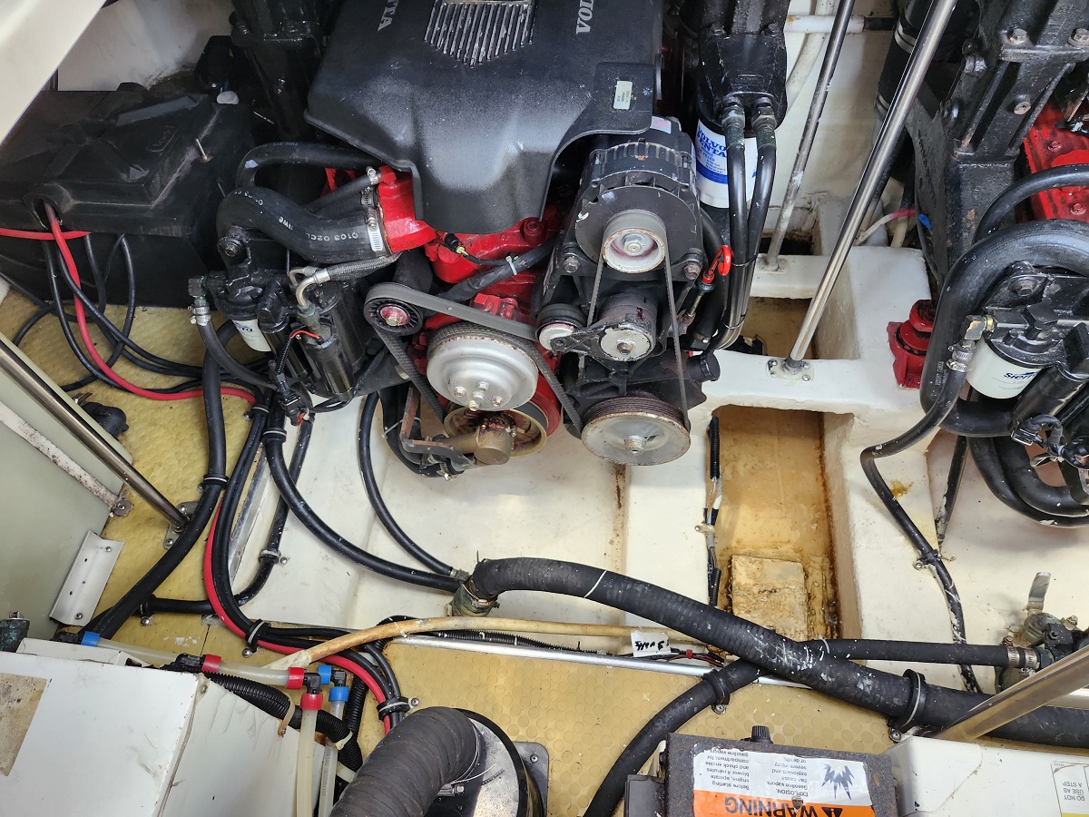 Boat engine bay with a red-and-black V-style engine, belts, pulleys, hoses, and wiring visible on a yellow deck.