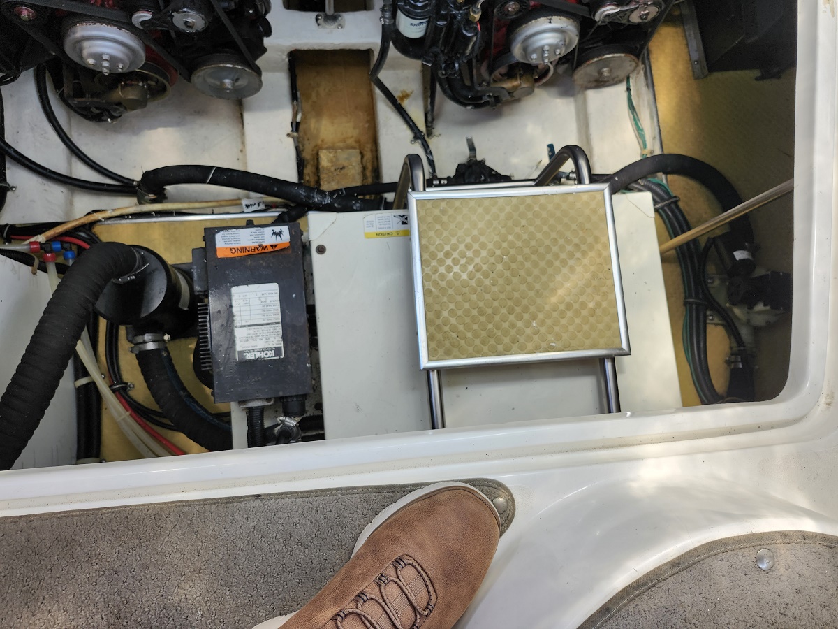view of boat engine compartment with battery, air filter, hoses and wiring; a person’s boot at the edge of the hatch