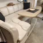 Cream-colored leather salon on a boat with a beige oval table, straw hat on the backrest, and black patterned cushions