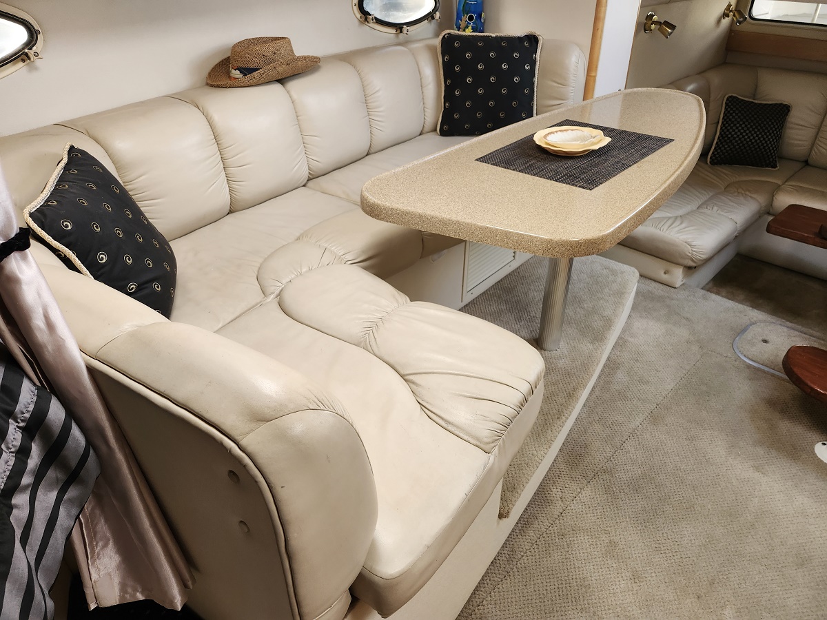 Cream-colored leather salon on a boat with a beige oval table, straw hat on the backrest, and black patterned cushions