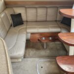 L-shaped beige leather sofa in a boat cabin, with a small wood table featuring two cup holders in front of it.