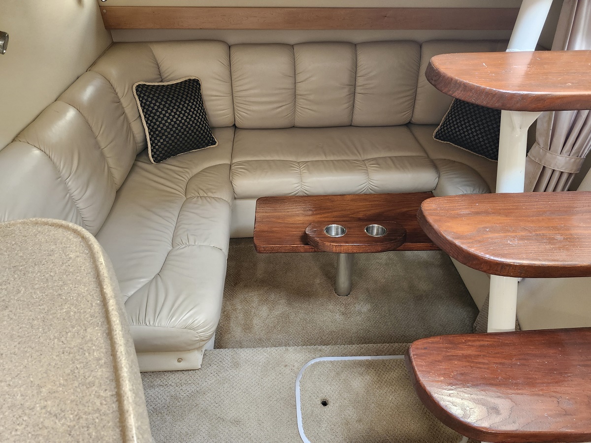 L-shaped beige leather sofa in a boat cabin, with a small wood table featuring two cup holders in front of it.