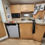 Boat galley with wooden cabinets, microwave, mini fridge, and a curved beige countertop with a sink.