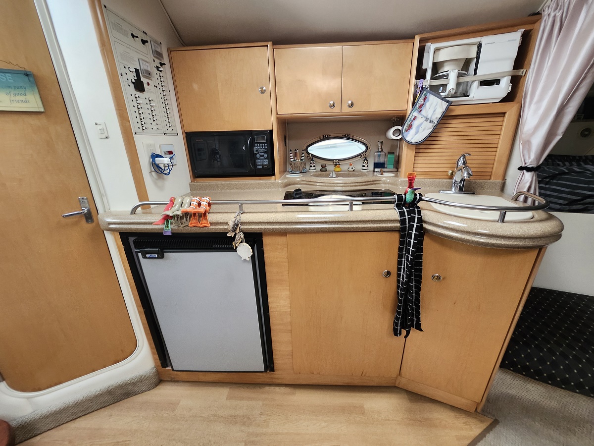 Boat galley with wooden cabinets, microwave, mini fridge, and a curved beige countertop with a sink.