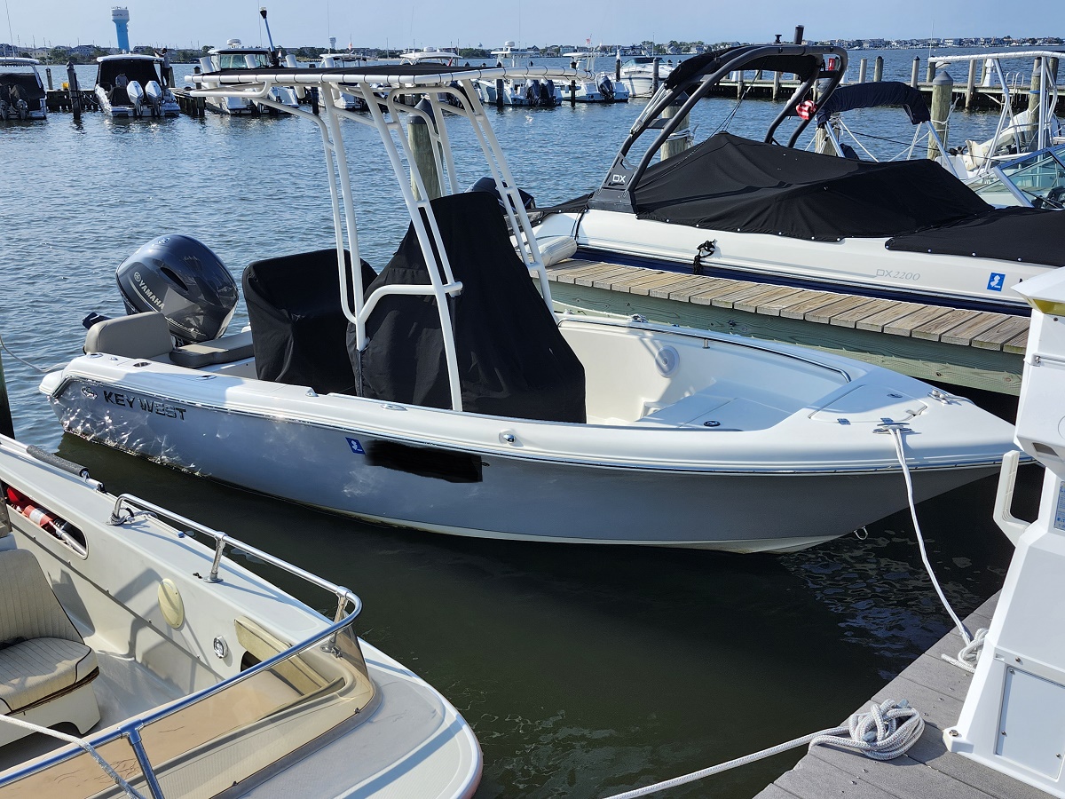 White Key West motorboat docked at a marina beside a covered speedboat and calm water.