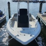 White motorboat moored at a wooden dock in a sunny marina, with a tall central console and ropes securing it.