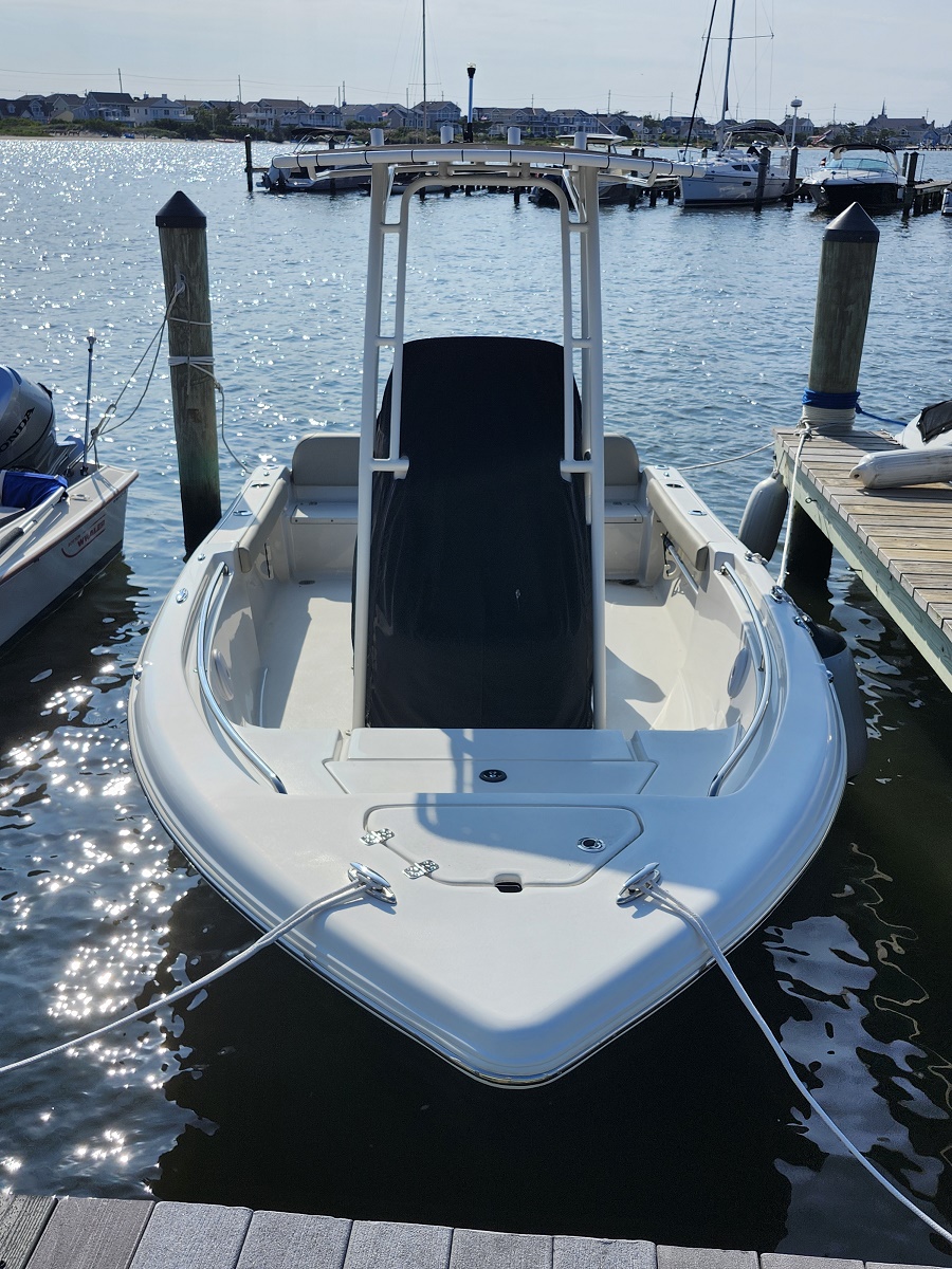 White motorboat moored at a wooden dock in a sunny marina, with a tall central console and ropes securing it.