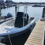 White powerboat tied to a wooden dock in a calm marina, center console with a black cover and an outboard motor visible on the stern.