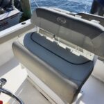 Gray boat seat with a KW logo on the backrest, mounted on a white deck with water in the background and another boat nearby by the dock