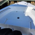 White boat cockpit with an open deck hatch, stainless steel rails along the sides, and a dock in the background under bright sunlight.