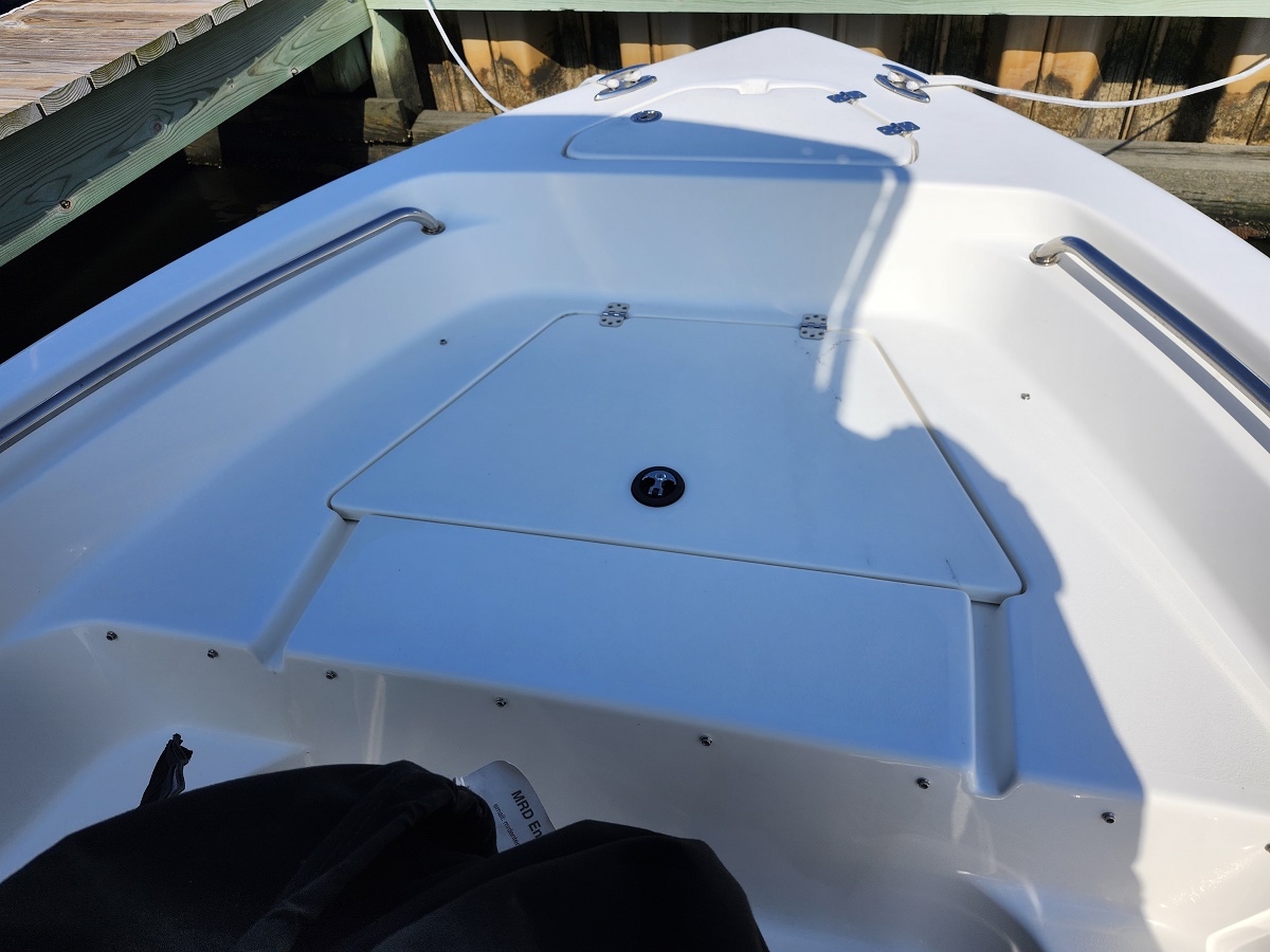 White boat cockpit with an open deck hatch, stainless steel rails along the sides, and a dock in the background under bright sunlight.